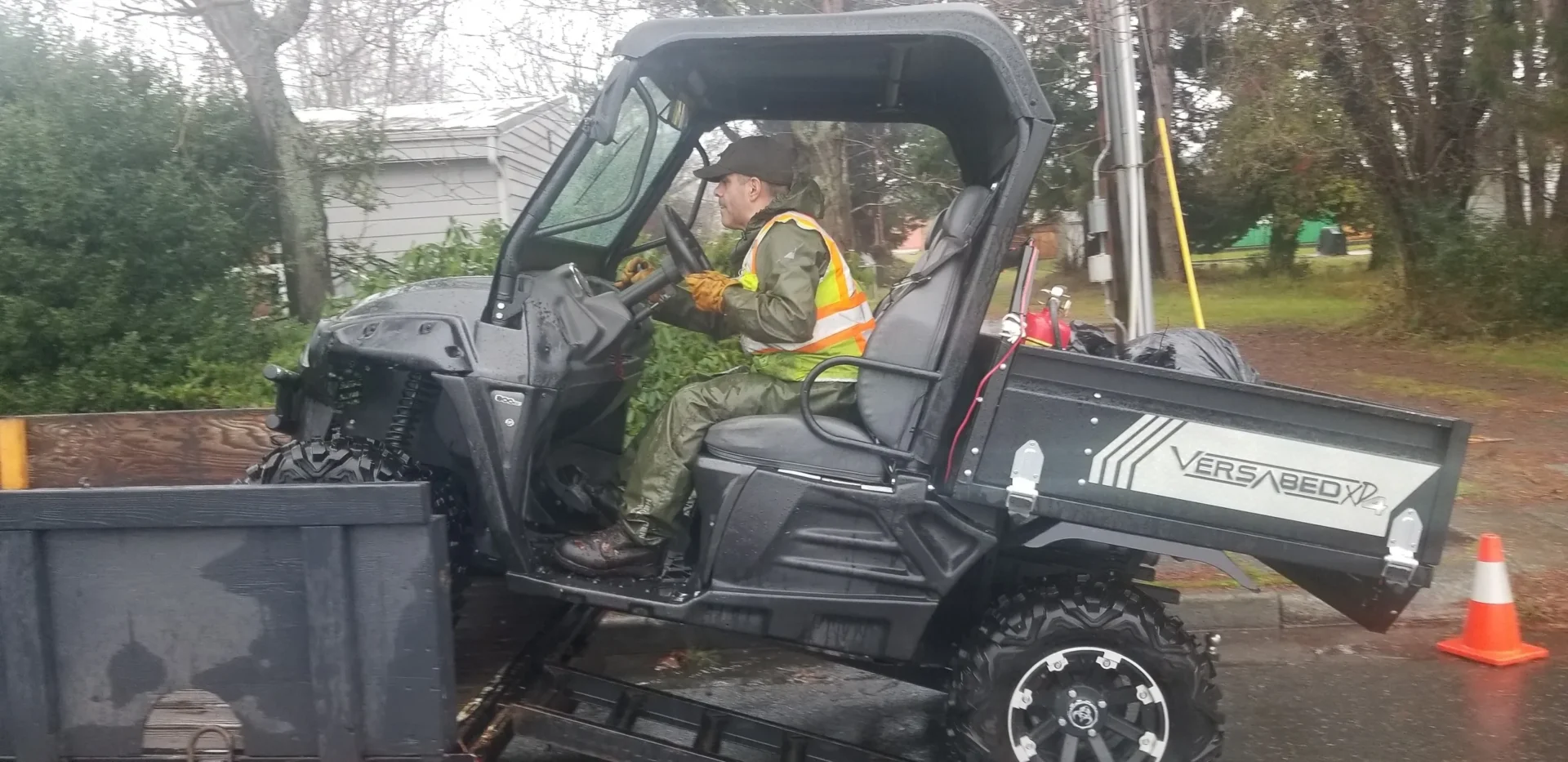 A man in green jacket sitting on the back of a black utility vehicle.