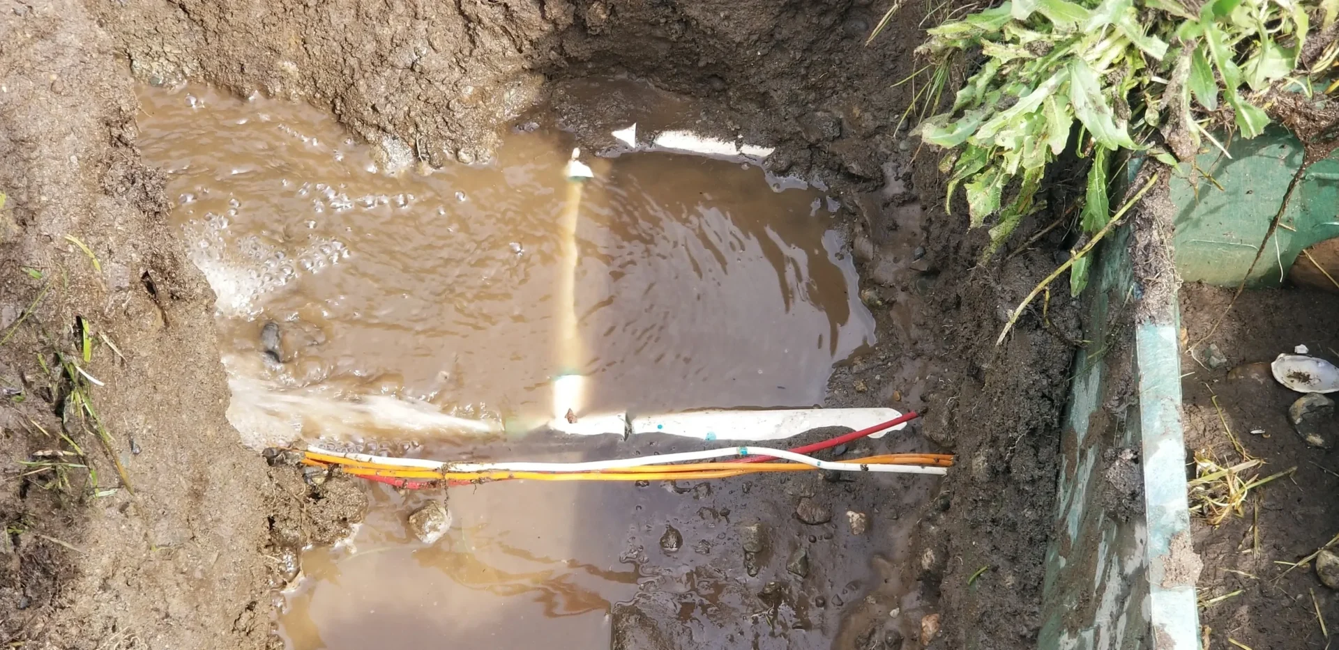 A pipe in the mud with water coming out of it.